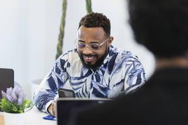 Smiling businessman using mobile phone at office - PNAF01179