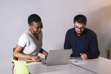 Male and female colleagues with laptop working on document in office - PNAF01181