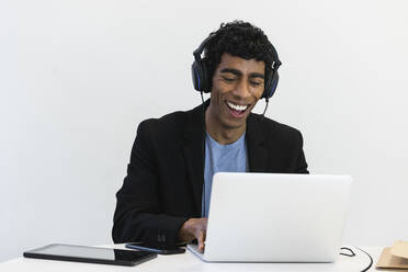 Cheerful businessman with headset attending video call over laptop at office - PNAF01191