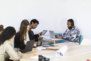 Geschäftsleute bei der Arbeit, während sie mit Kollegen in einem kreativen Büro sitzen - PNAF01208