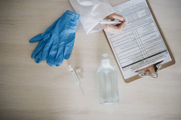 Eine Ärztin schreibt einen Bericht auf einem Klemmbrett neben medizinischen Geräten am Schreibtisch - EBBF02796