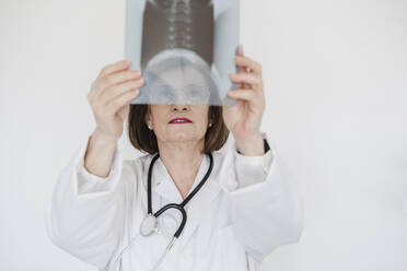 Ältere Ärztin, die ein Röntgenbild vor einer weißen Wand untersucht - EBBF02806
