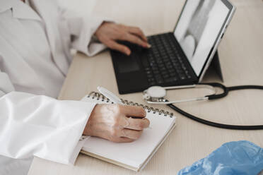 Ärztin, die ein digitales Tablet benutzt, während sie am Schreibtisch in einer medizinischen Klinik Tagebuch schreibt - EBBF02811