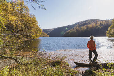 Woman standing on shore of Rursee reservoir on sunny autumn day - GWF06938