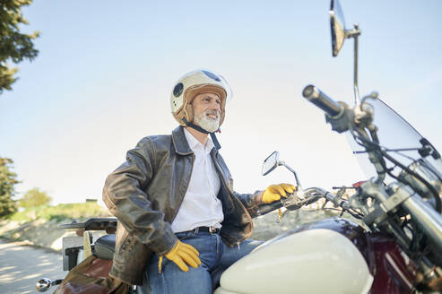 Smiling man looking away while sitting on motorcycle - KIJF03670