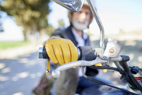 Älterer Mann mit gelben Handschuhen, der den Lenker eines Motorrads hält, während er auf dem Motorrad sitzt - KIJF03671