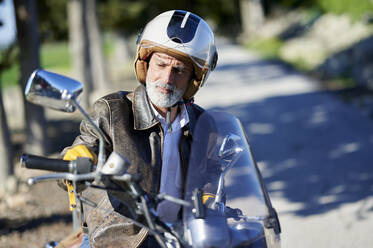 Thoughtful man wearing helmet sitting on motorcycle - KIJF03673