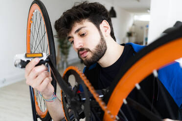 Mann hält Pedal, während er ein umgestürztes Fahrrad zu Hause betrachtet - GIOF11917