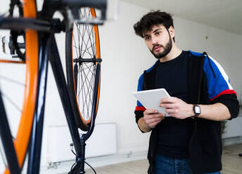 Mann schaut auf ein umgestürztes Fahrrad, während er ein digitales Tablet zu Hause hält - GIOF11921