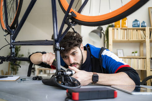 Young man repairing bicycle seat at home - GIOF11930