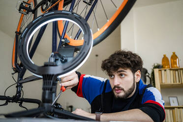 Männlicher Informant schaut auf sein Smartphone, während er zu Hause sein Fahrrad repariert - GIOF11942