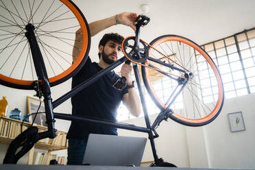 Mann mit Laptop, der zu Hause Fahrradpedale dreht - GIOF11956