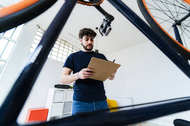 Junger Mann schreibt Notizen, während er zu Hause neben einem umgestürzten Fahrrad steht - GIOF11959