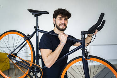 Lächelnder Mann mit Fahrrad auf der Schulter zu Hause - GIOF11969