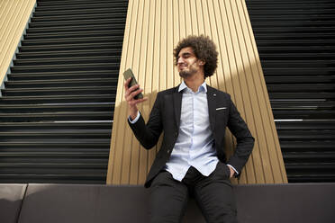 Afro man using smart phone while leaning on wall during sunny day - VEGF04091