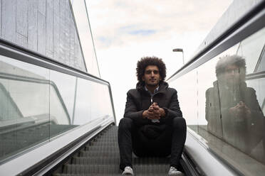 Gutaussehender Afro-Mann sitzt auf Rolltreppe am Himmel - VEGF04109