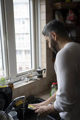 Man cleaning plate in kitchen at home - FBAF01646