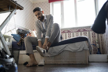 Geschäftsmann trägt Schuhe, während er zu Hause auf dem Bett sitzt - FBAF01648