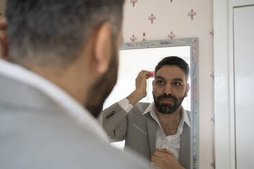 Bearded businessman looking at reflection in mirror at home - FBAF01657