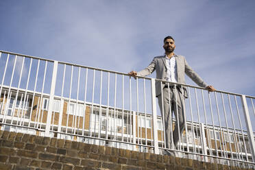 Thoughtful businessman looking away while standing at railing on footbridge - FBAF01664