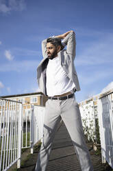 Businessman with arms raised looking away while standing on footbridge - FBAF01666