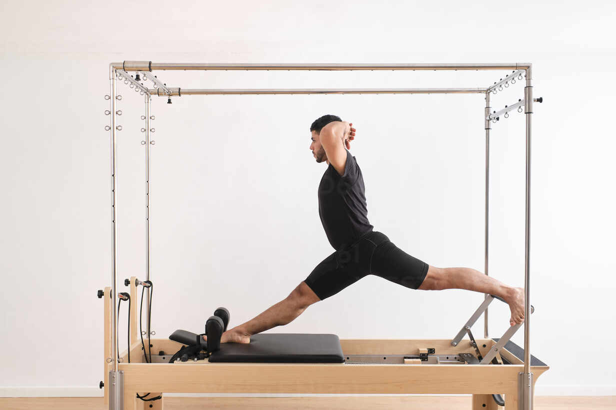 Male athlete with hands behind head practicing pilates on cadillac reformer  in exercise room stock photo