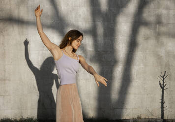 Woman with arms raised dancing against wall - AXHF00220