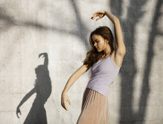 Beautiful young woman dancing by wall during sunny day - AXHF00222
