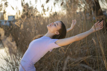 Young woman with arms raised dancing in nature - AXHF00229