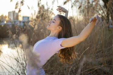 Beautiful young woman with arms raised dancing in nature - AXHF00230