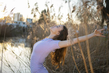 Flexible Frau tanzt in der Nähe von See in der Natur - AXHF00231