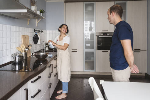 Lächelnde Frau im Gespräch mit ihrem Mann bei der Zubereitung von Speisen in der Küche zu Hause - VYF00419