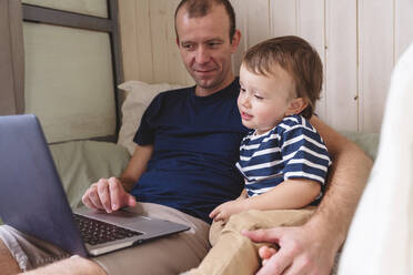 Vater arbeitet am Laptop, während er mit seinem Sohn im Heimbüro sitzt - VYF00448