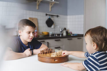 Geschwister spielen Schach am Esstisch in der Küche zu Hause - VYF00461