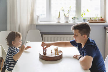 Junge spielt Schach mit jüngerem Geschwisterkind am Tisch zu Hause - VYF00462