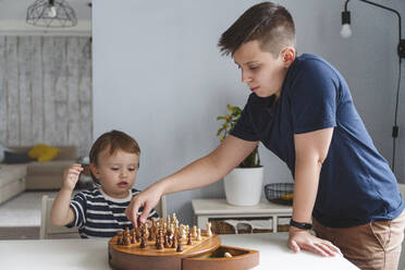 Geschwister spielen Schach auf einem Tisch in einer modernen Wohnung - VYF00463