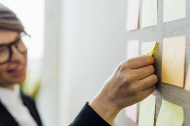 Businesswoman sticking adhesive note on wall in office - MEUF02203