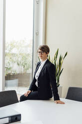 Geschäftsfrau sitzt auf dem Schreibtisch im Büro - MEUF02205