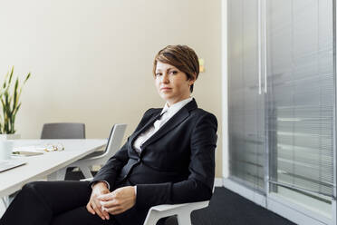 Weibliche Unternehmerin mit leerem Blick sitzt auf einem Stuhl im Büro - MEUF02226