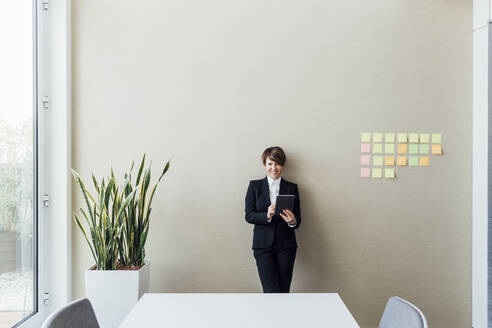 Lächelnde Unternehmerin, die ein digitales Tablet an die Wand im Büro hält - MEUF02231