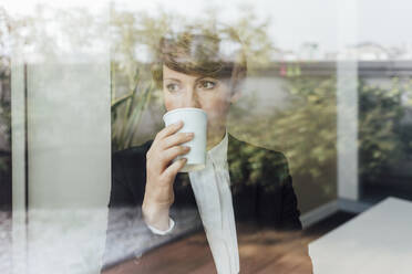 Nachdenkliche Unternehmerin, die Kaffee trinkt und wegschaut, gesehen durch ein Glasfenster - MEUF02242