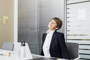 Tired female entrepreneur with eyes closed relaxing on chair at desk in office - MEUF02268