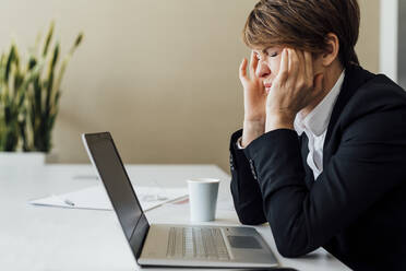 Frustrated female business professional sitting in front of laptop at desk - MEUF02271