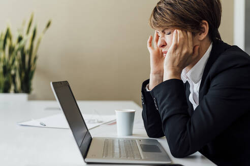 Frustrierte Geschäftsfrau, die vor einem Laptop am Schreibtisch sitzt - MEUF02271