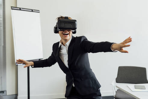 Cheerful female business professional with virtual reality simulator in office - MEUF02287