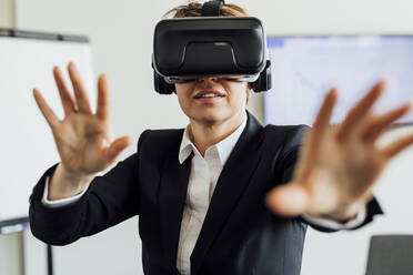 Geschäftsfrau gestikuliert, während sie einen Virtual-Reality-Simulator im Büro trägt - MEUF02288