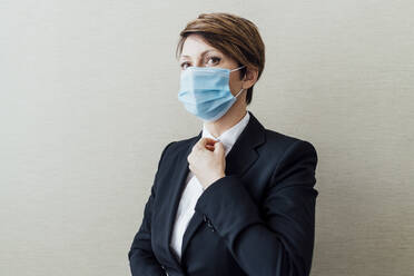 Weiblicher Geschäftsmann mit Gesichtsschutzmaske vor einer Wand während COVID-19 - MEUF02295
