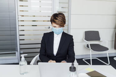 Geschäftsfrau mit Gesichtsschutzmaske bei der Arbeit am Laptop im Büro - MEUF02302