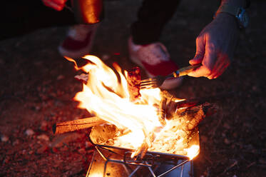 Mann brät Fleisch über Holzofen beim nächtlichen Camping - JCMF01945