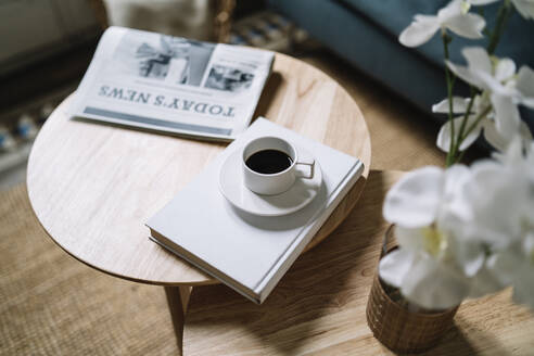 Coffee on book by newspaper on wooden table at home - JCZF00542